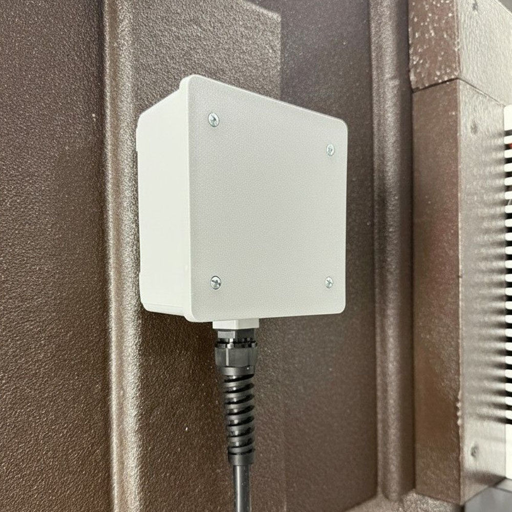 A white rectangular electrical junction box with four mounting screws, mounted on the Freedom Cooler with a black cable connector below.