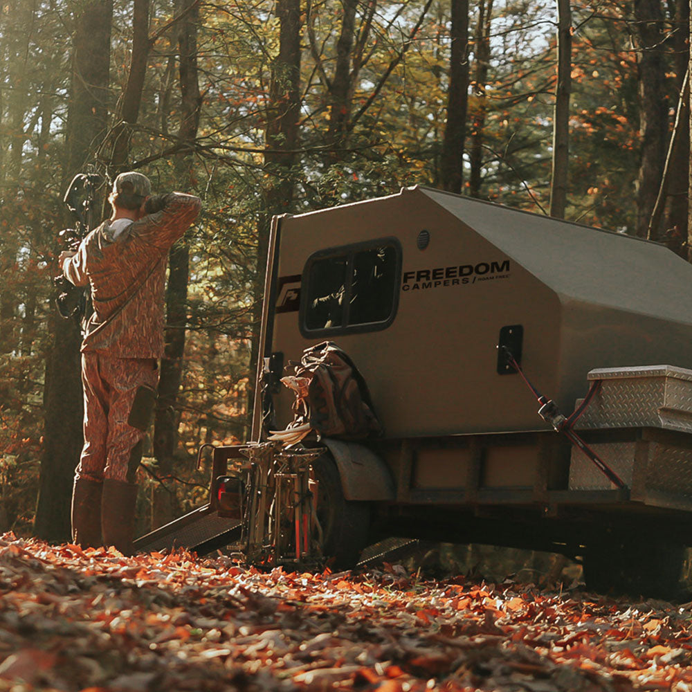 A hunter next to his camper shooting a boow in the woods.